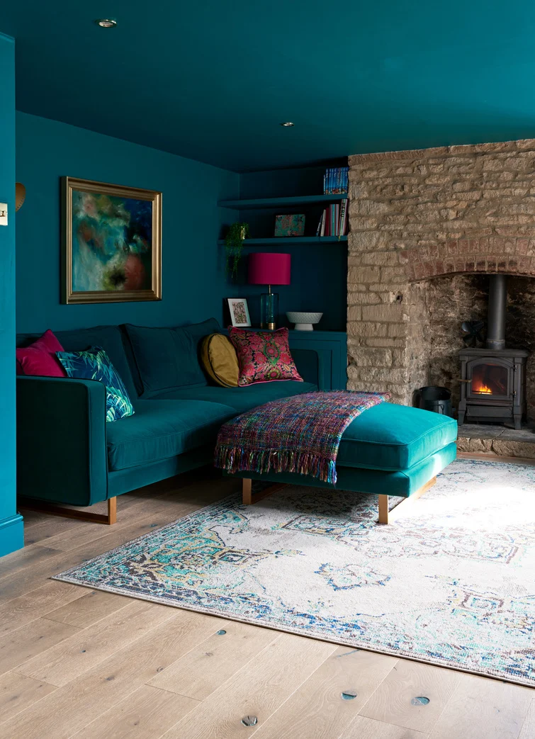 Home Transformation a bold and cosy living space featuring vibrant teal walls and matching sofa with an original stone brick fireplace.