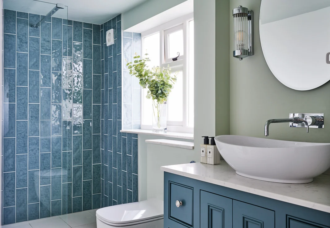 Home transformation the bathroom renovation has a serene colour palette of sage green walls and cornflower blue tiles, finished with greenery and a large round mirror.