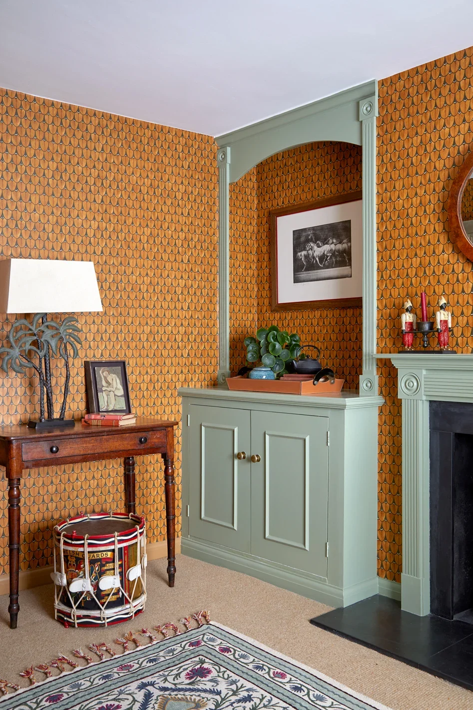 Remodelling rooms: a cosy living space with warm orange patterned wallpaper, a sage green built in cabinet and decorative moulding.