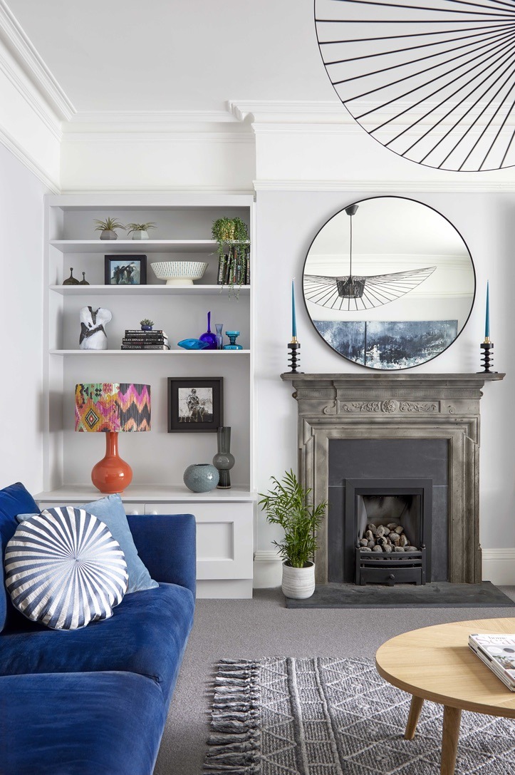 Modern design in a traditional house with a royal blue sofa, built in alcoves, round feature mirror and the original fireplace.