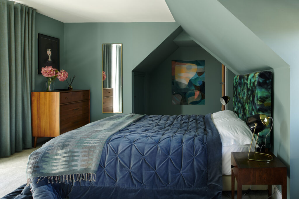 1950s Dormer Bungalow serene bedroom renovation with soft green walls, deep blue tufted velvet bedspread, and bold abstract headboard.