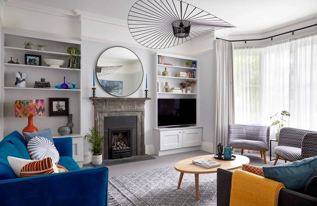 Modern design in a traditional house: a cosy living area with two sofas, built in alcove shelves either side of the original fireplace, furnished with a patterned rug and wooden coffee table.