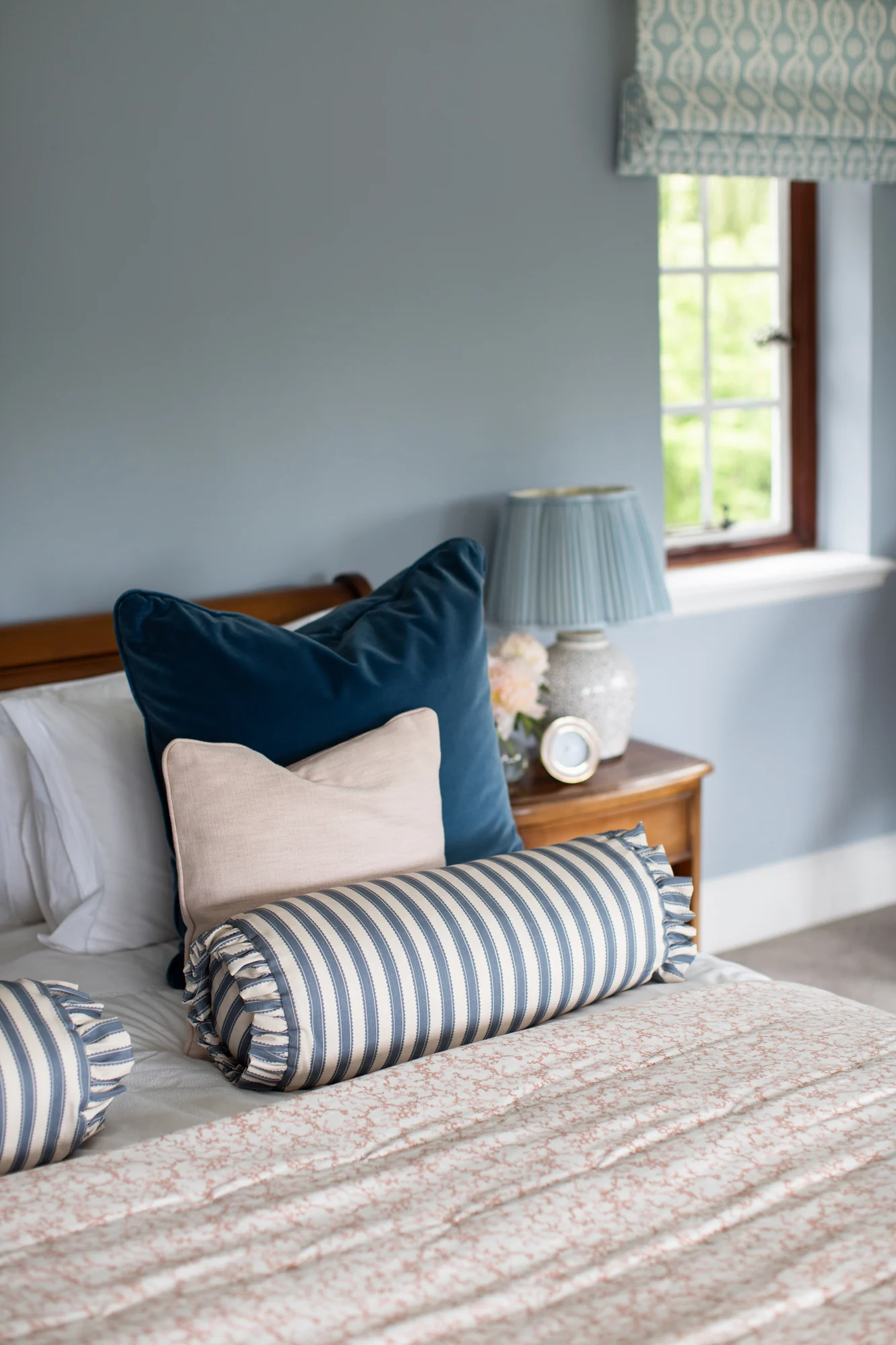 Garden‑inspired interior design guest bedroom with soft bedding, floral artwork, and large windows framing garden views.