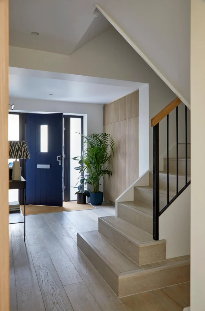 Renovating your home: light and airy hallway with blue front door, black metal staircase, and warm oak flooring for a fresh, modern welcome.