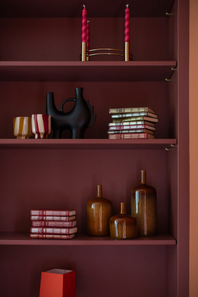 Kate Lovejoy Interiors has styled this shelf as part of a clients long-term design relationship, maroon red coats the bespoke fitted cabinetry while books and trinkets add decoration