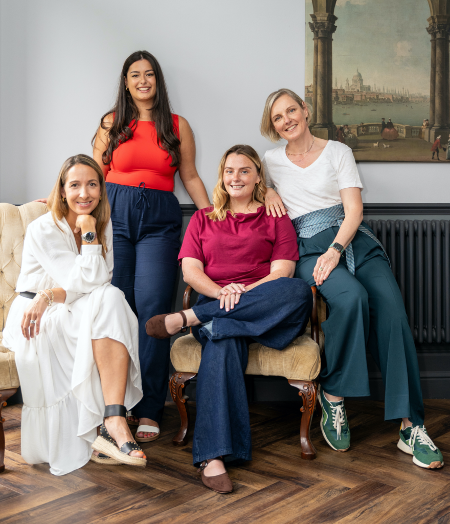 About Kate Lovejoy Interiors - The Team of 4 ladies posed on and around a cream chez long