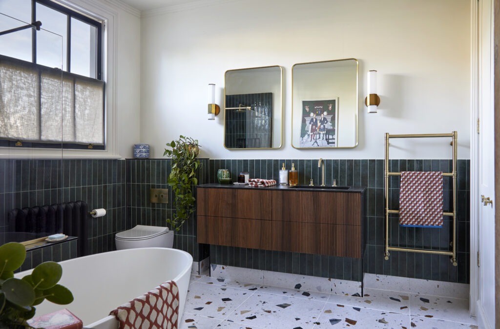 Contemporary bathroom with dark green tiles, terrazzo flooring, wood vanity and brass accents.