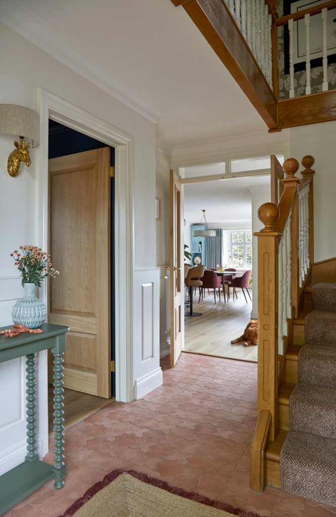 Open-plan hallway designed by Kate Lovejoy Interiors in Maidenhead, looking into the kitchen-living space, featuring an oak staircase, oak doors, and an olive green sidetable.