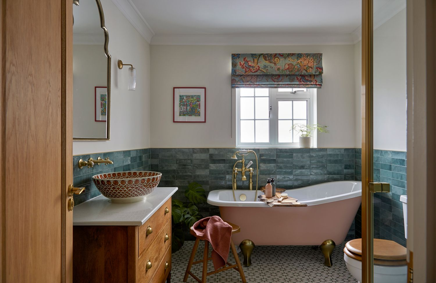 Kate Lovejoy Interiors showcasing a modern bathroom with teal walls, a pink bath, warm wooden cabinetry, and textured tiled flooring.
