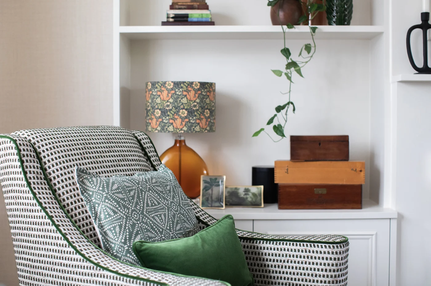 A softly lit reading corner with a linen armchair positioned beside a window, natural light filtering through sheer curtains, a wooden side table stacked with books, and a woven wool throw — an example of an intentional, analog space designed for slower living.